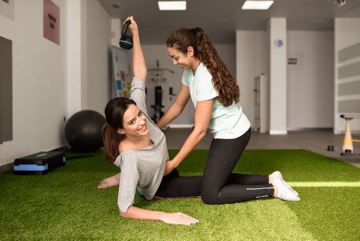 Physical therapist assisting young caucasian woman with exercise with dumbbell during rehabilitation in the gym at hospital. Female physiotherapist training a patient in physiotherapy center.