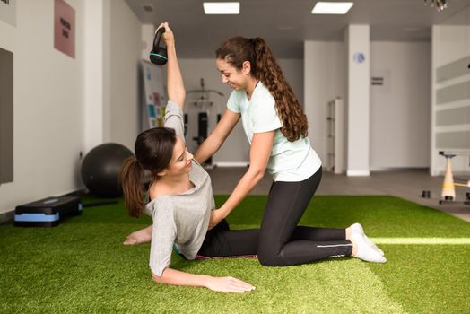 Physical therapist assisting young caucasian woman with exercise with dumbbell during rehabilitation in the gym at hospital. Female physiotherapist training a patient in physiotherapy center.