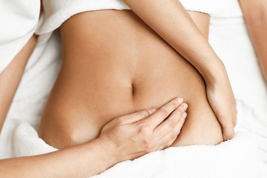 Top view of hands massaging female abdomen.Therapist applying pressure on belly. Woman receiving massage at spa salon