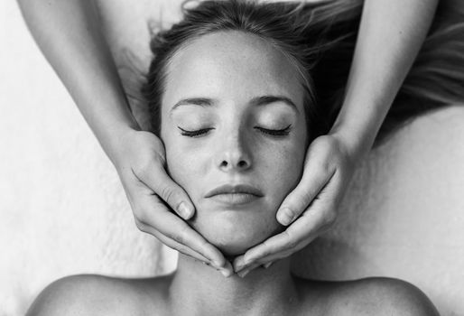 Young blond woman receiving a head massage in a spa center with eyes closed. Female patient is receiving treatment by professional therapist.