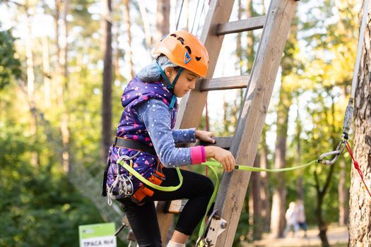 Girl climbing in adventure park is a place which can contain a wide variety of elements, such as rope climbing exercises, obstacle courses and zip-lines.