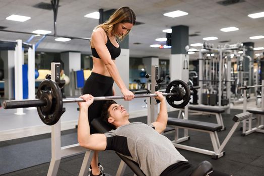 Female personal trainer helping a young man lift weights while working out in a gym