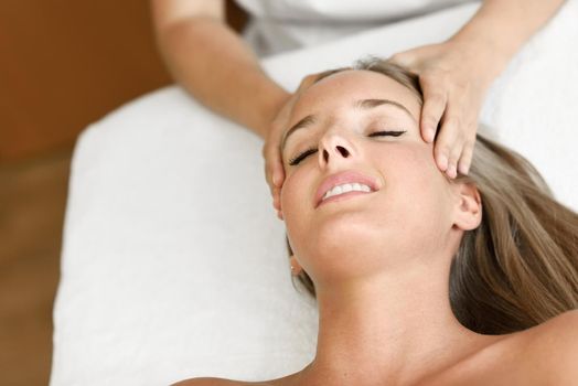 Young blond woman receiving a head massage in a spa center with eyes closed. Female patient is receiving treatment by professional therapist.