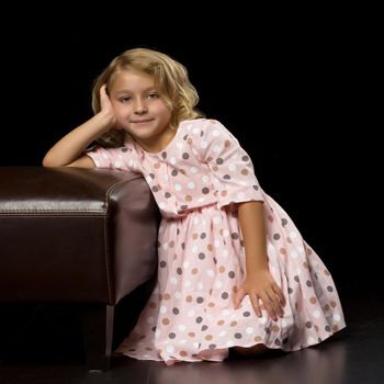 Cute little girl put her head on her hand, she was thinking about something on a black background.