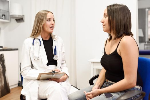 Female doctor explaining diagnosis to her patient. Brunette woman having consultation with blonde girl in medical office.