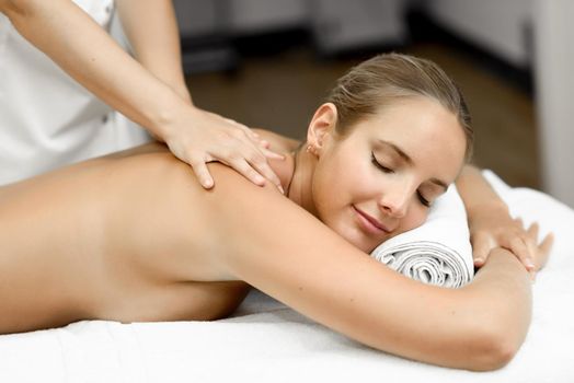 Young blond woman having massage in the spa salon. Massage and body care. Body massage treatment. Smiling female.