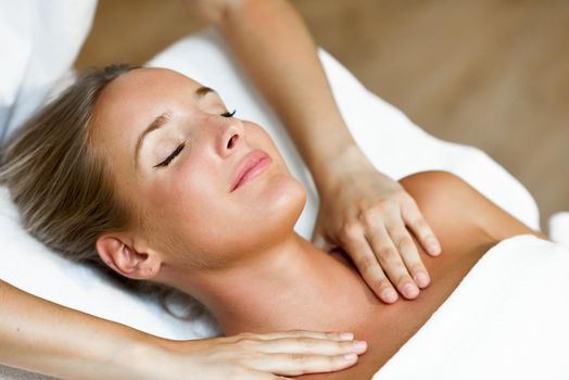 Young blond woman receiving a head massage in a spa center with eyes closed and smiling. Female patient is receiving treatment by professional therapist.