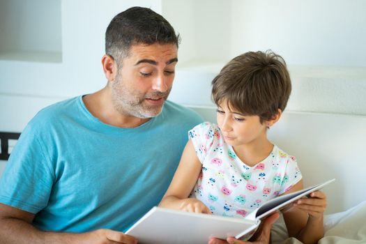 Funny dad and lovely little girl are having fun on the bed. Middle-age father with her eight years daughter using digital tablet in bedroom.