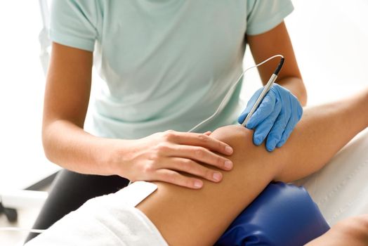 Electroacupuncture dry with needle connecting machine used by acupunturist on female patient for acupuncture guided by EPI Intratissue Percutaneous Electrolisis. Electro stimulation in physical therapy to knee of a young woman in physiotherapy center.