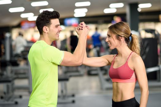 Smiling young man and woman doing high five in gym. Couple wearing sportswear