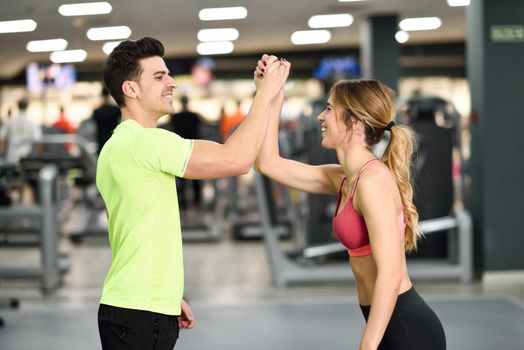 Smiling young man and woman doing high five in gym. Couple wearing sportswear