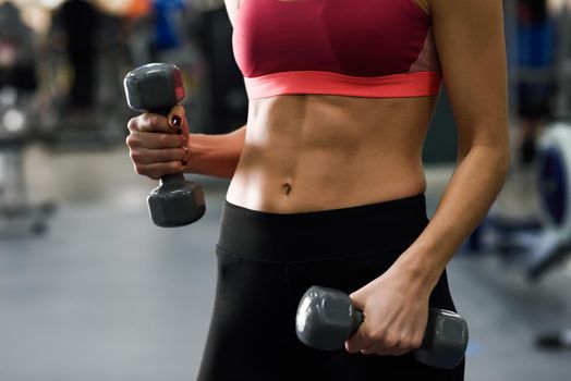 Young woman with beautiful abdomen lifting dumbells at gym. Girl wearing sportswear clothes.