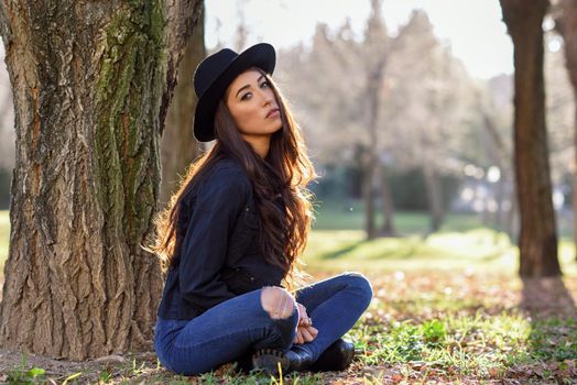 Portrait of thoughtful woman sitting alone outdoors wearing hat. Nice backlit with sunlight