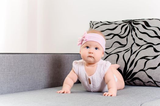 Portrait of a baby girl with a bandage and a bow on her head on a sofa. Beautiful child with blue eyes