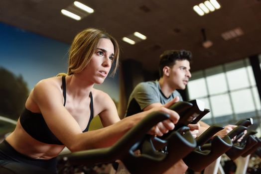 Attractive woman and man biking in the gym, exercising legs doing cardio workout cycling bikes. Couple in a spinning class wearing sportswear.