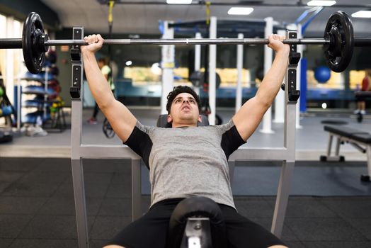 Young man bodybuilder doing weight lifting in gym. Attractive man wearing sportswear