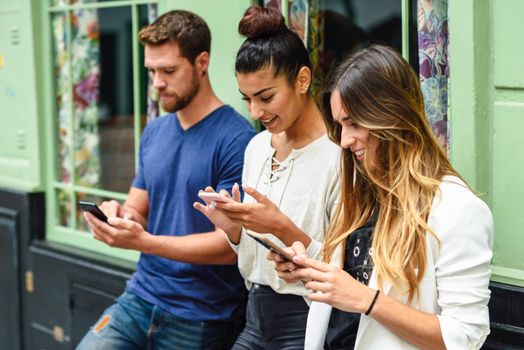 Multiethnic group of three people looking down at smart phone smiling, concepts about technology addiction and youth