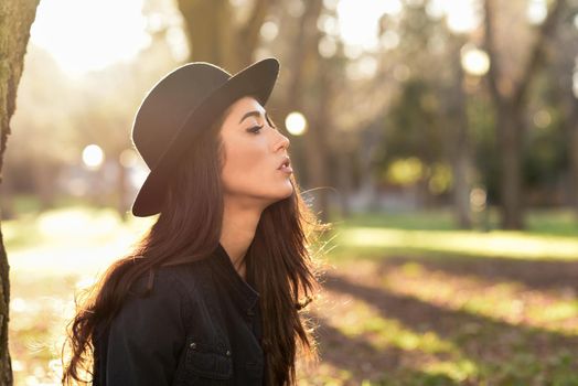 Portrait of thoughtful woman sitting alone outdoors wearing hat. Nice backlit with sunlight