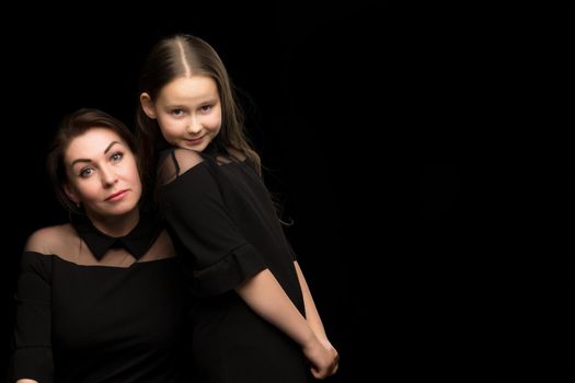 Happy family mom and daughter in the studio on a black background. The concept of love, childhood.