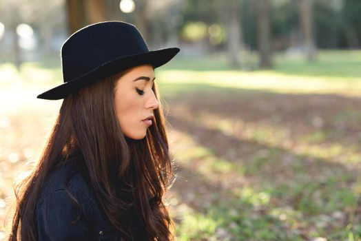 Portrait of thoughtful woman sitting alone outdoors wearing hat. Nice backlit with sunlight