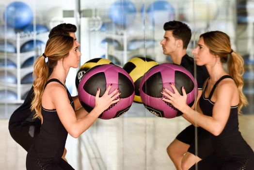 Man and Woman lifting fitballs in the gym. Young people wearing sportswear clothes in front of a mirror.