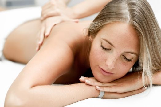 Young blond woman having massage in the spa salon. Massage and body care. Body massage treatment.