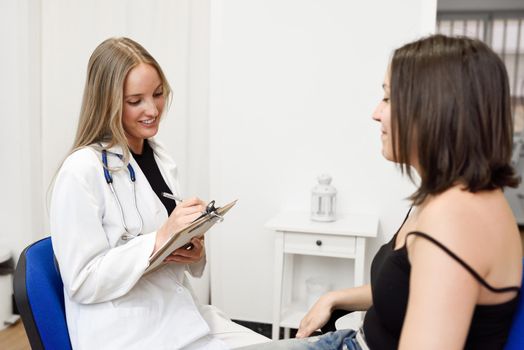Female doctor explaining diagnosis to her patient. Brunette woman having consultation with smiling blonde girl in medical office.