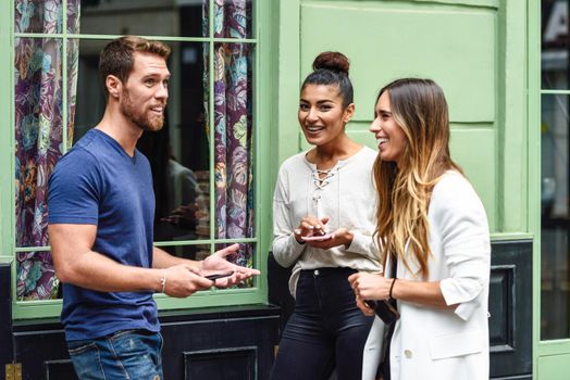 Three multiethnic people talking and smiling outdoors with smart phone in their hands. Multiracial group of friends in urban background.