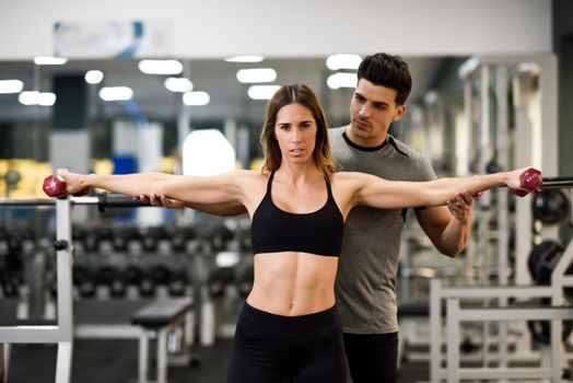 Personal trainer helping a young woman lift dumbells while working out in a gym