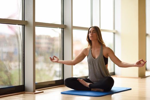 Young beautiful woman meditating in the lotus position in gym. Girl wearing sportswear clothes.