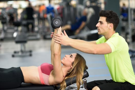 Personal trainer helping a young woman lift weights while working out in a gym