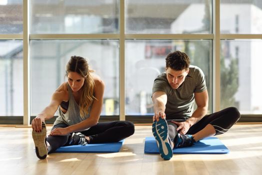 Young woman and man working out indoors. Two people streching their legs on the floor of a gym.