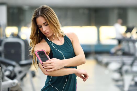 Young woman using smartphone standing in the gym before the training.