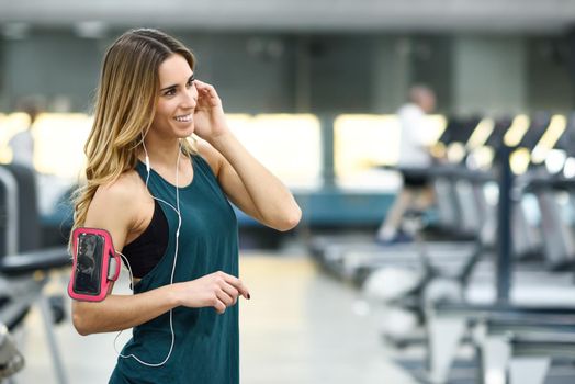 Young woman using smartphone standing in the gym before the training. Beautiful girl smiling.