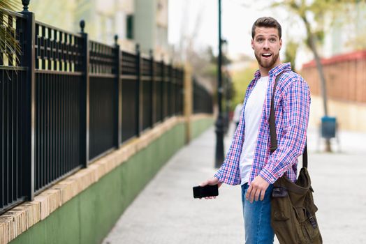 Young bearded man surprised in urban background. Tourist wearing casual clothes. Lifestyle concept.