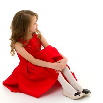 Portrait of Cute Preteen Girl Sitting on the Floor with Her Knees Up, Adorable Girl with Blond Long Hair Wearing Red Fashionable Dress Posing Looking to the Side in Studio on Isolated White Background