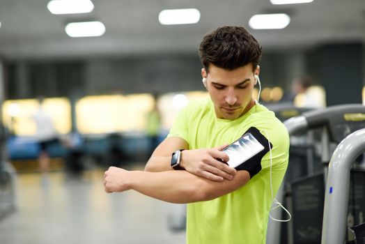 Young man using smartphone standing in the gym before the training. Attractive male with smartwatch