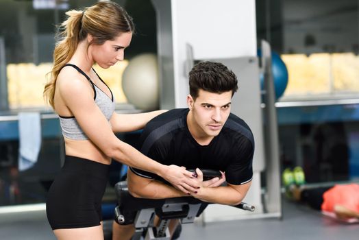 Female personal trainer helping a young man lift weights while working out in a gym