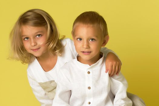 The older sister and younger brother are hugging in the studio on a Yellow background. Childhood concept.