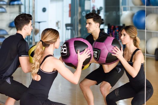 Man and Woman lifting fitballs in the gym. Young people wearing sportswear clothes in front of a mirror.