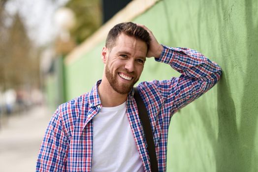 Attractive young man laughing outdoors. Funny guy wearing casual clothes in urban background. Lifestyle concept.