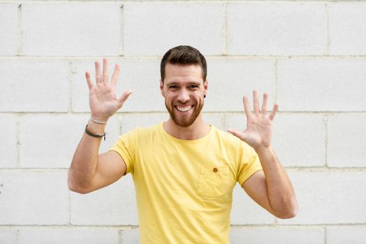 Funny young man on brick wall with open hands smiling. Guy wearing casual clothes in urban background.