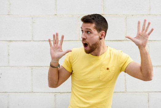 Funny young man on brick wall with open hands looking at leftside. Guy wearing casual clothes in urban background.