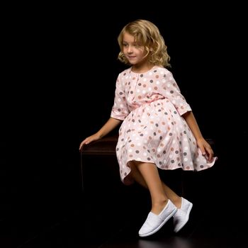 Beautiful little girl, studio portrait on a black background. The concept of a happy childhood, style and fashion.