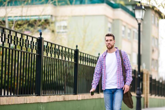 Young bearded man walking in urban background. Traveler wearing casual clothes. Lifestyle concept.