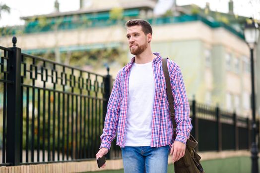 Young bearded man walking in urban background. Traveler wearing casual clothes. Lifestyle concept.