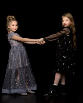 Two cute little girls are holding hands. Studio photography on a black background.