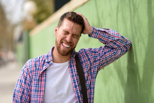 Attractive young man laughing outdoors. Funny guy wearing casual clothes in urban background. Lifestyle concept.