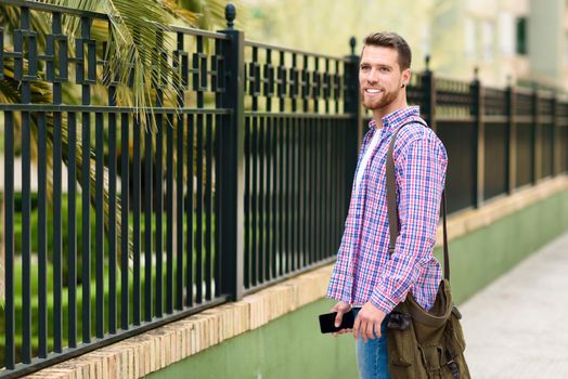 Young bearded man standing in urban background. Traveler wearing casual clothes. Lifestyle concept.