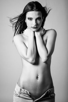 Beautiful young brunette woman wearing broken blue jeans. Beautiful topless girl with make up eyes and crossed arms. Studio shot.